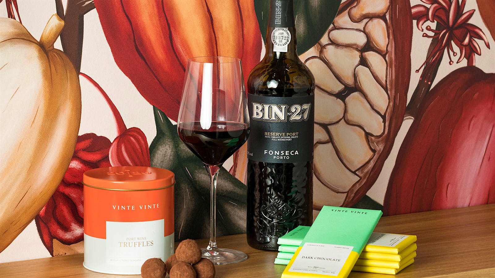 A bottle of Fonseca's Bin No. 27 Reserve Port, alongside a poured glass, Vinte Vinte chocolate truffles and dark chocolate bars