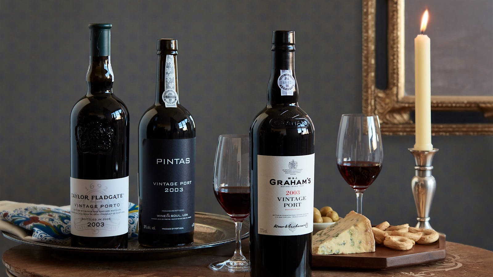 Three bottles of Vintage Port alongside two glasses of Port with a cheese board