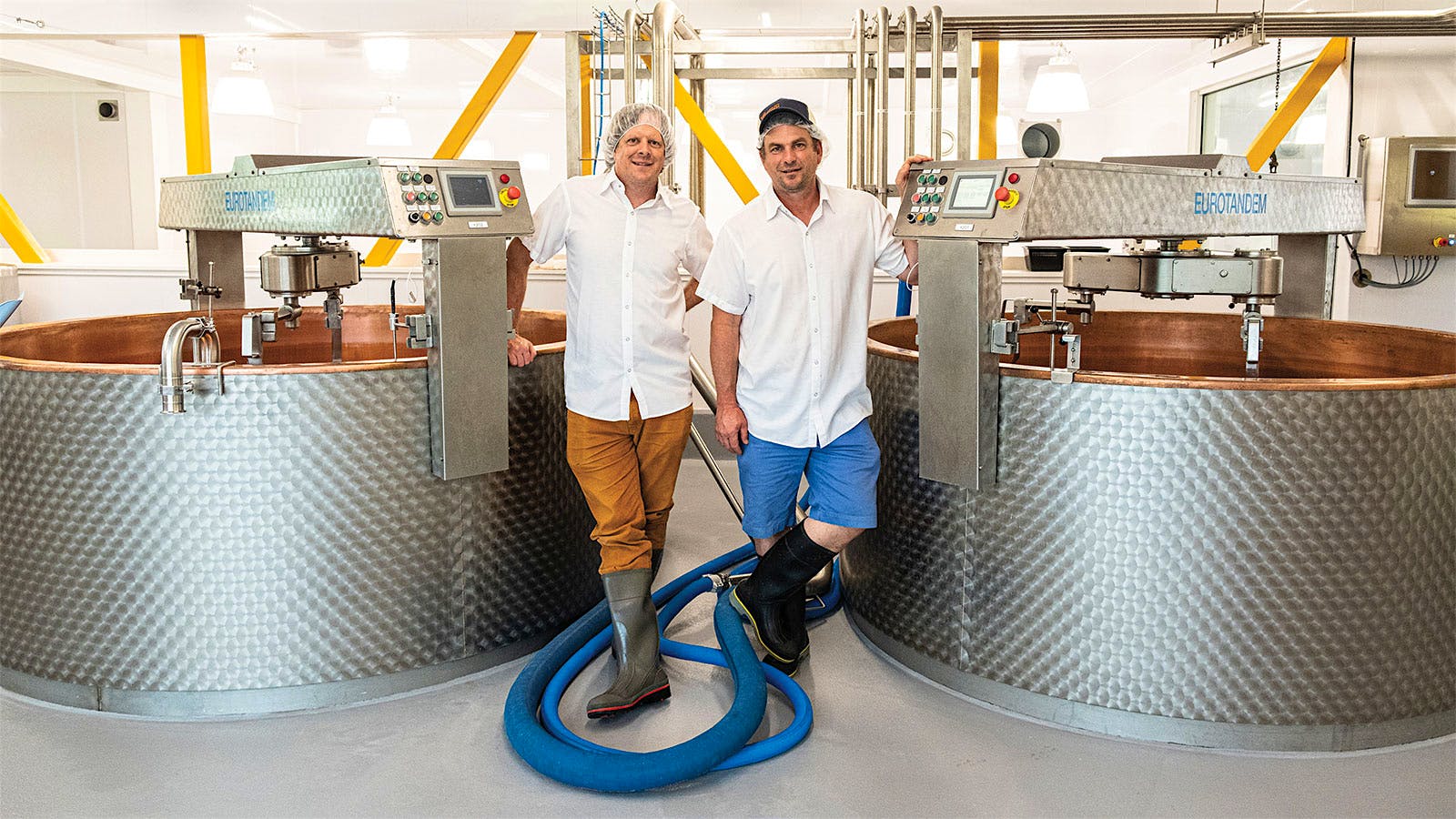 Andy (left) and Mateo Kehler stand next to two copper-lined vats at their cheesemaking farm, Jasper Hill.