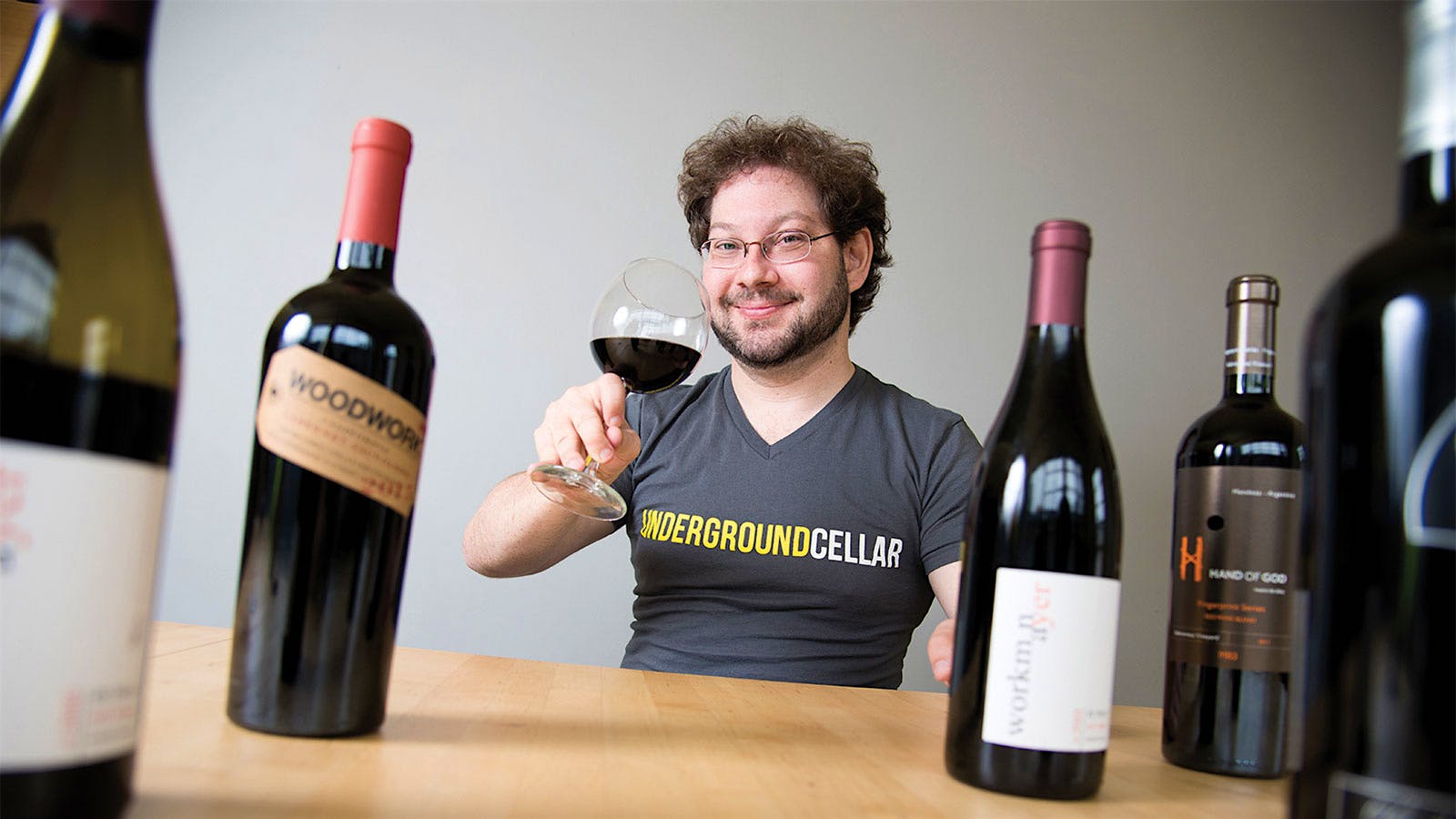 Underground Cellar’s founder Jeff Shaw with a glass of red wine and multiple bottles in front of him on a table