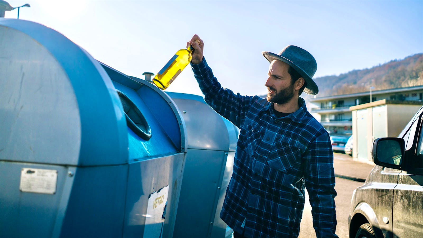  A person recyles a glass bottle by putting it in a recyling bin at a recyling plant.