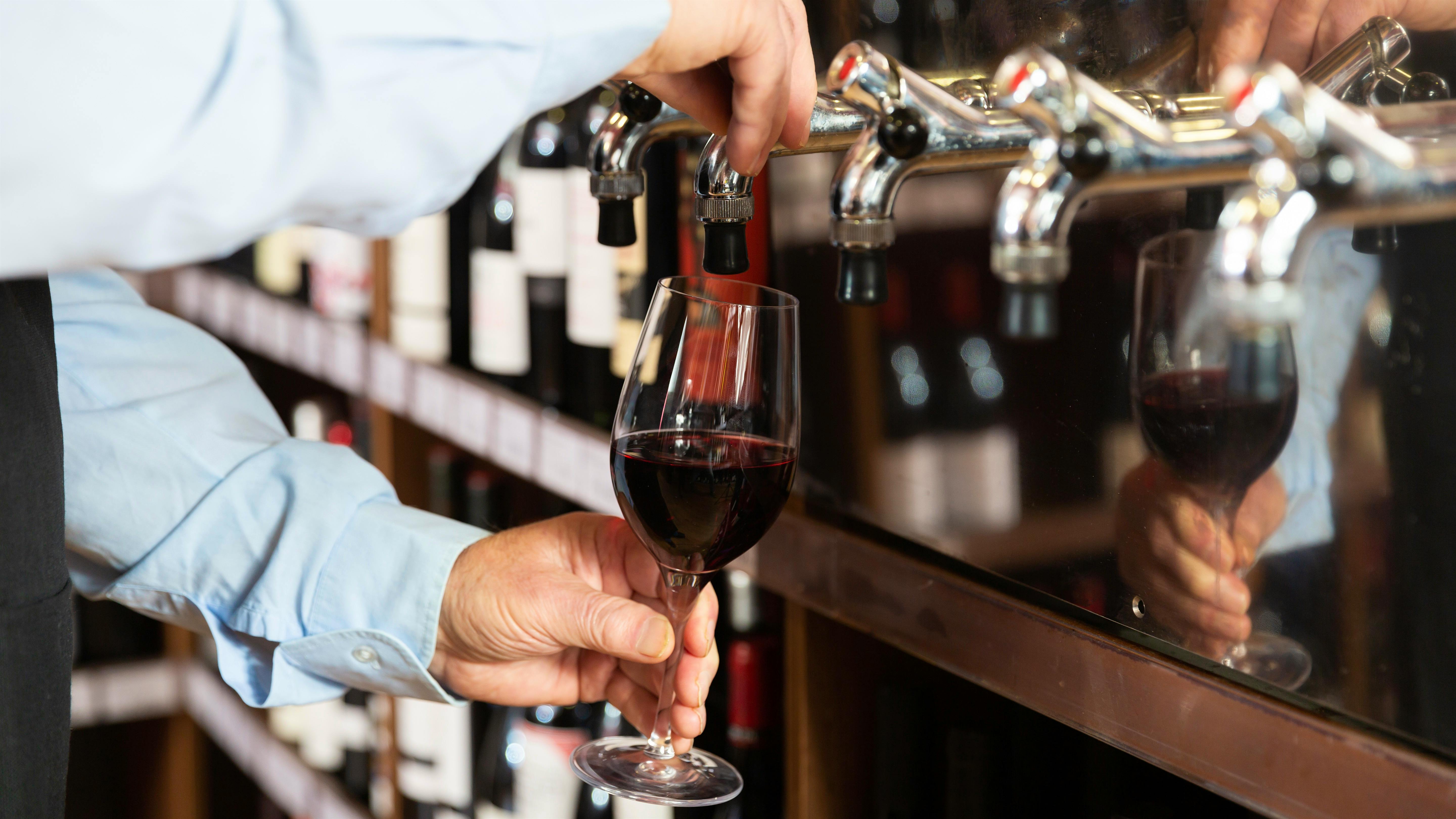  A person pours a glass of red wine into a glass from a tapped keg.