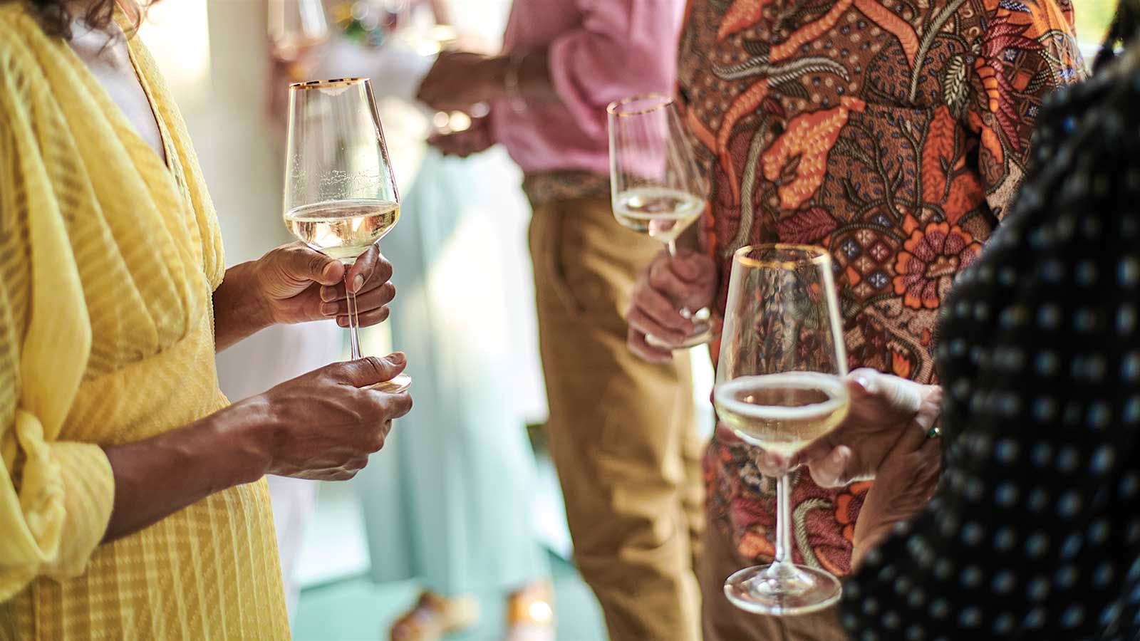 People stand with glasses of white sparkling wine in a crowd.