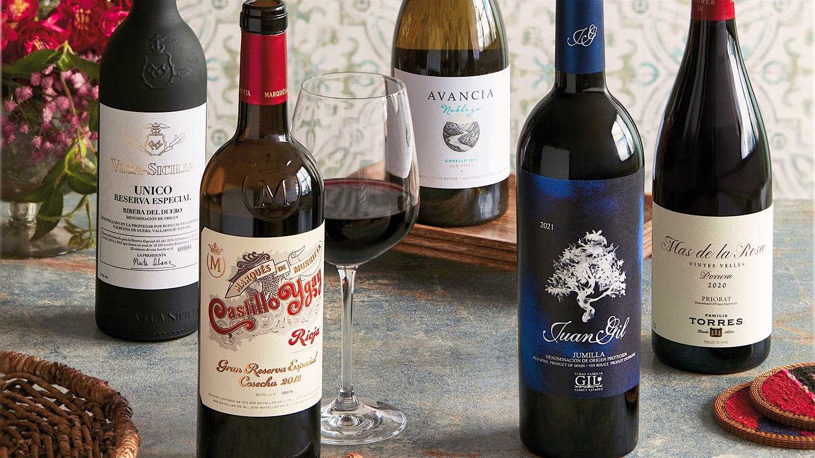 Five bottles of Spanish wines displayed on a table with a glass of red wine in the center.