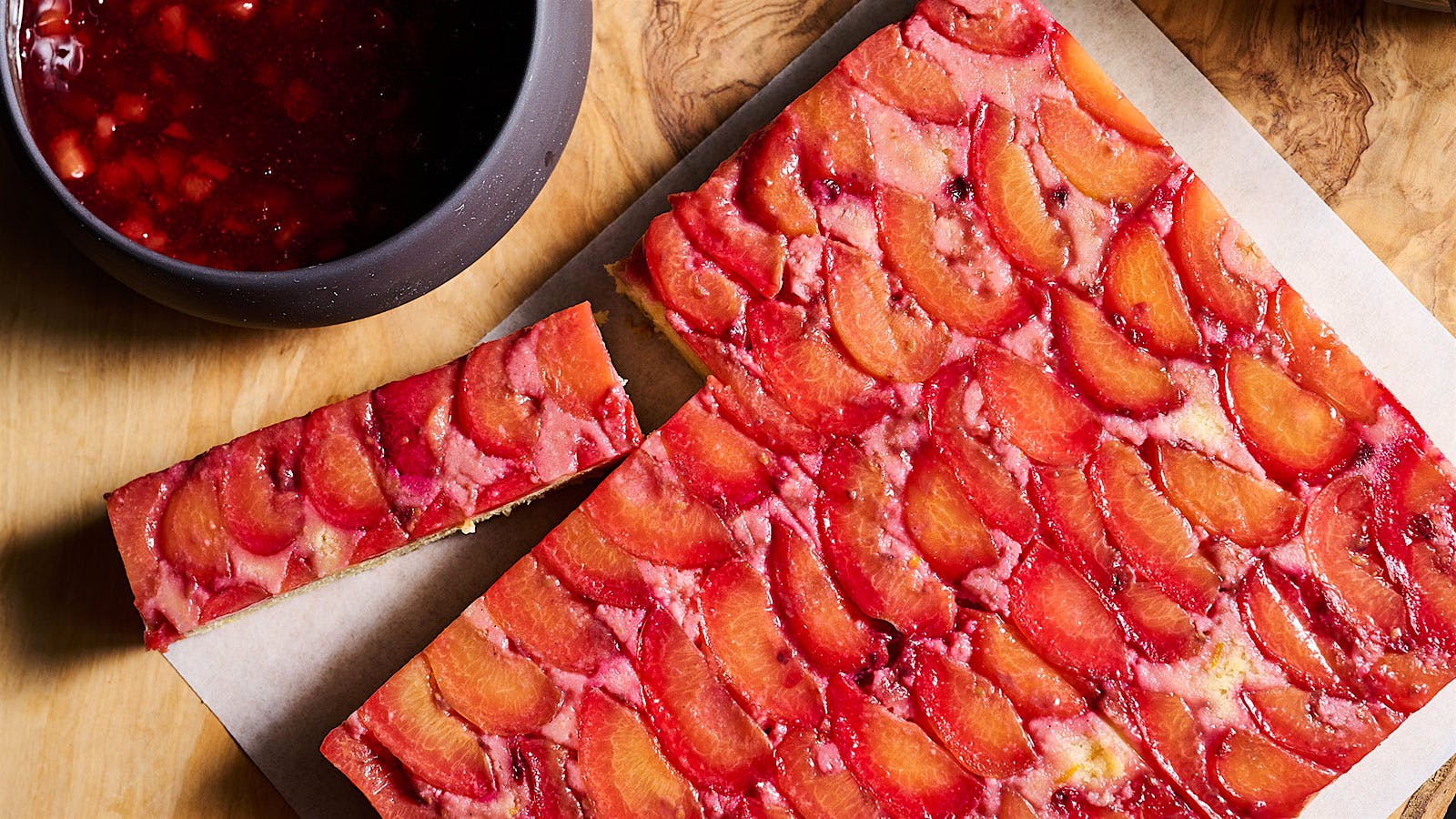 Plum cake, with one slice cut out, displayed next to a bowl of plum-orange sauce