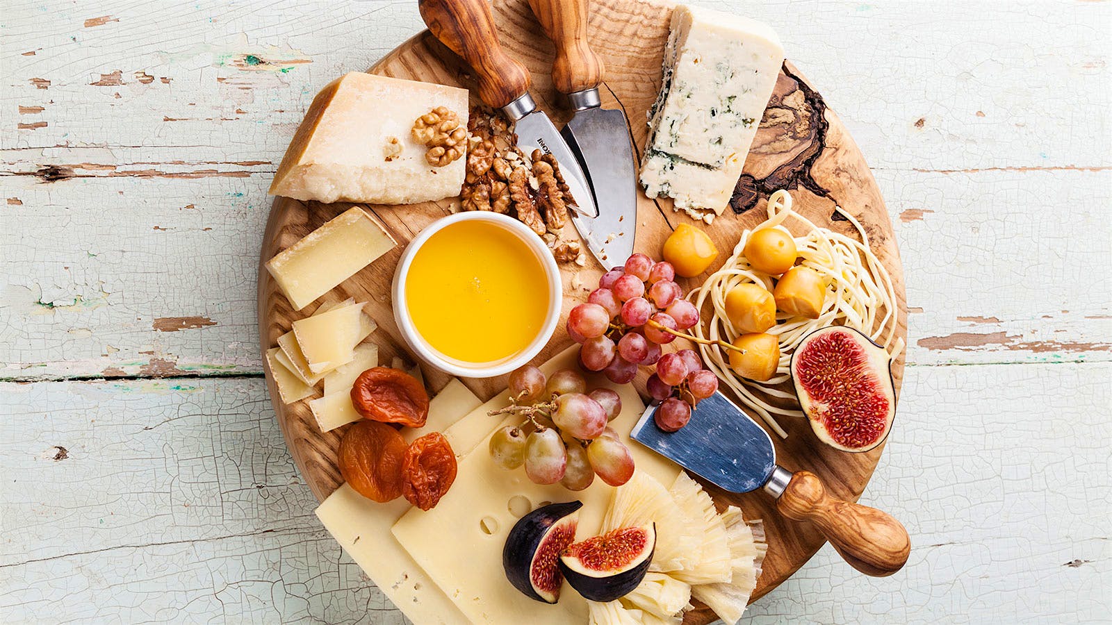 A cheese plate is displayed with figs, crackers, charcuterie and various cheese knives