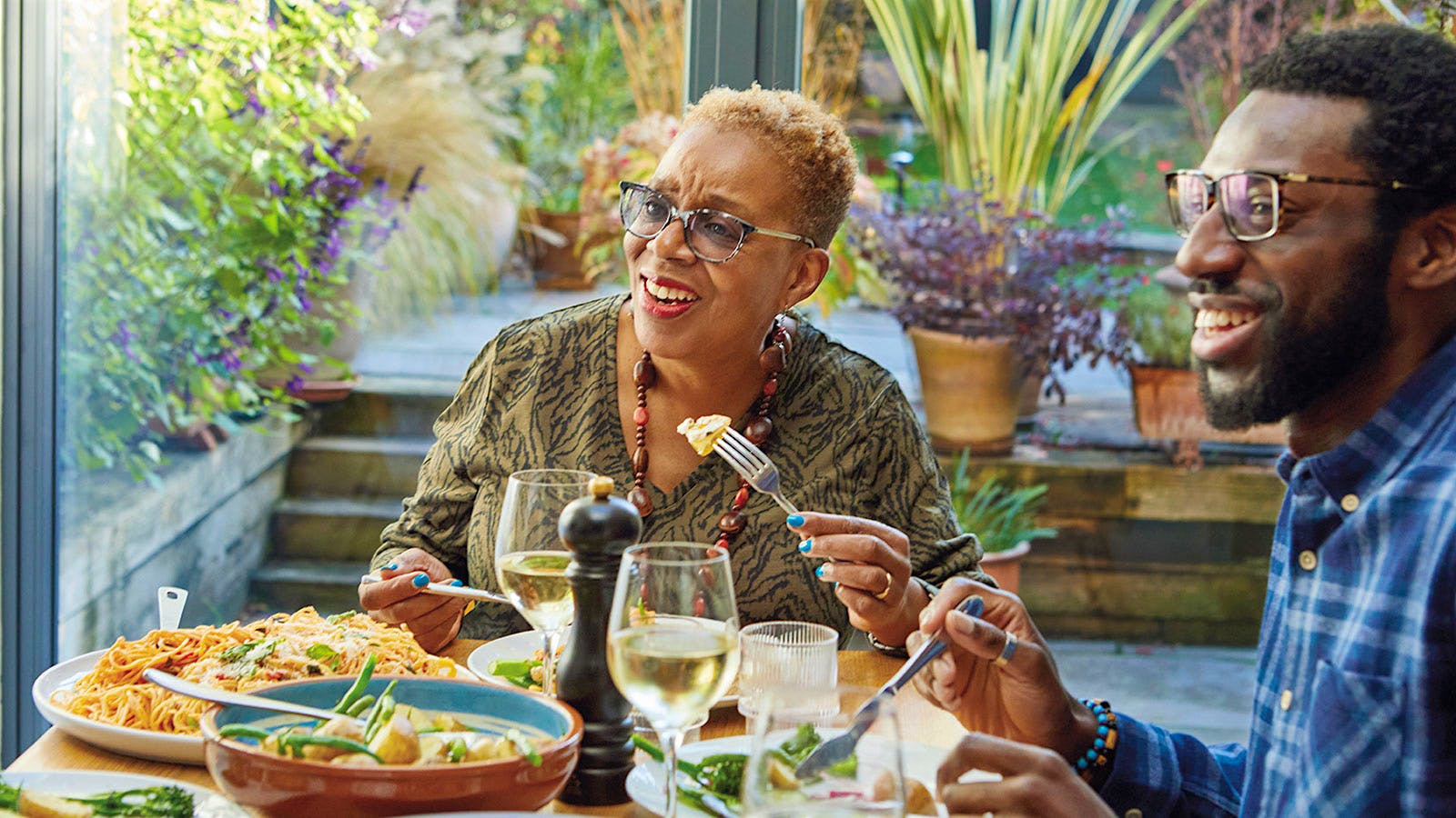 Two people eat a meal on a patio with glasses of white wine.