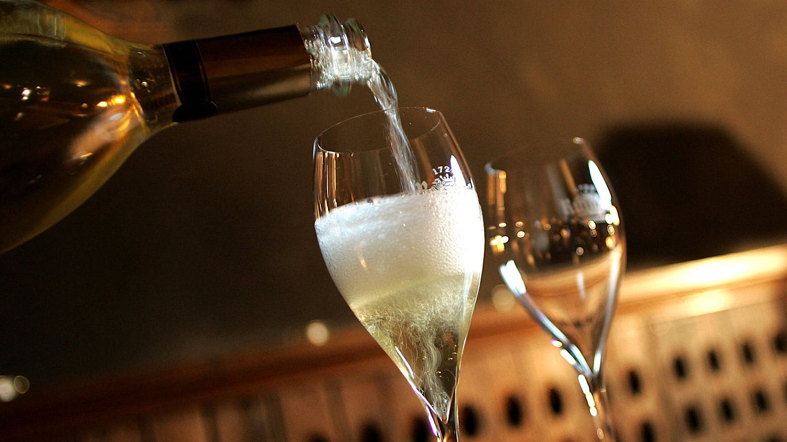 White sparkling wine is poured into teardrop flute glasses