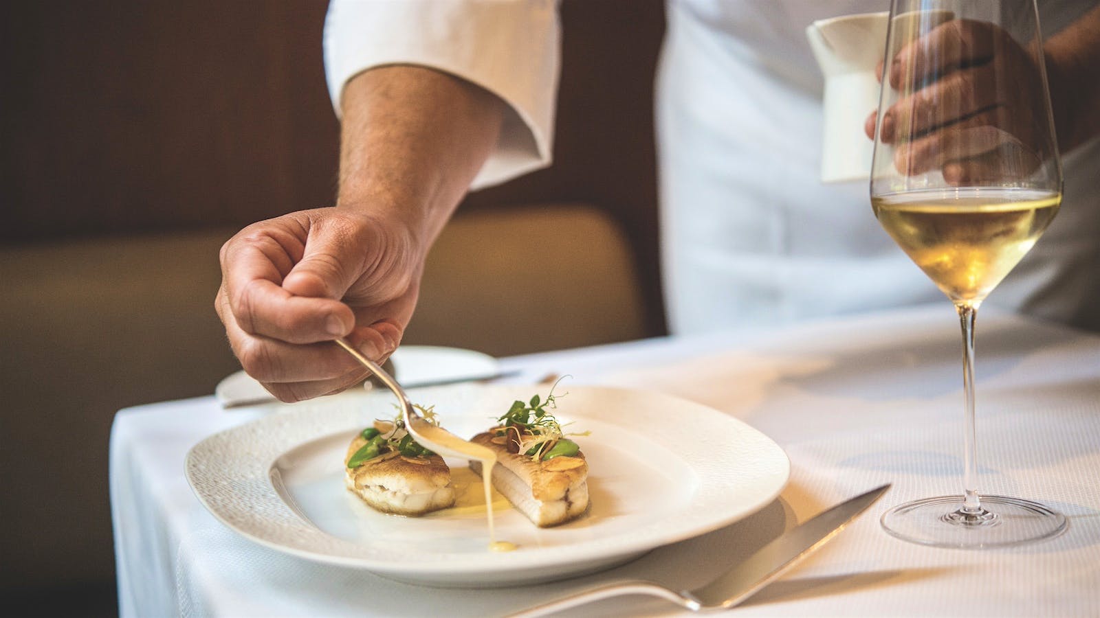 A chef dresses a plate of Dover sole with lemon potato mousseline and a shallot emulsion at a table alongside a glass of white wine at Le Bernardin in New York