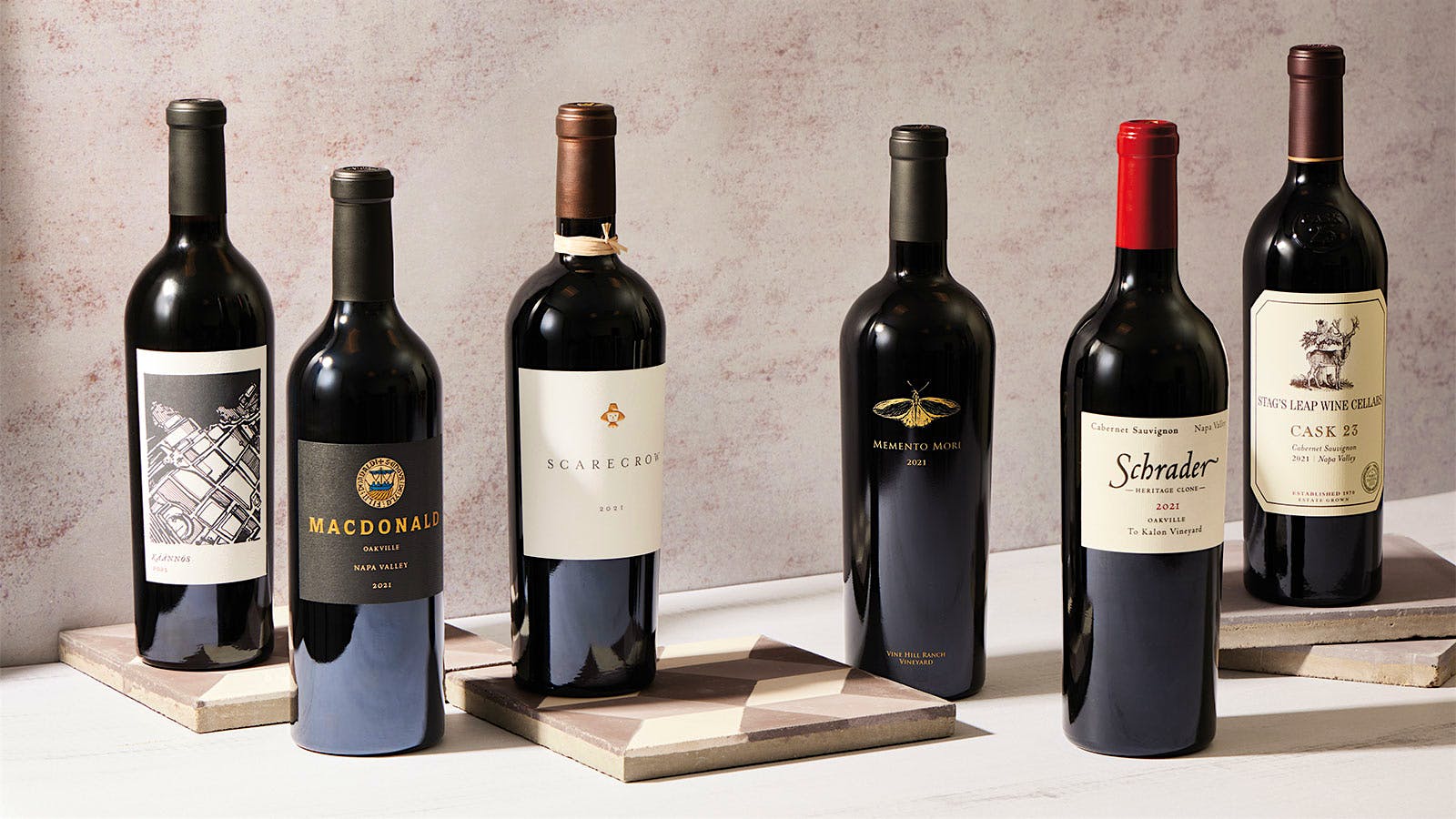 Six bottles of California Cabernet Sauvignon wines from the 2021 vintage are displayed on a table.