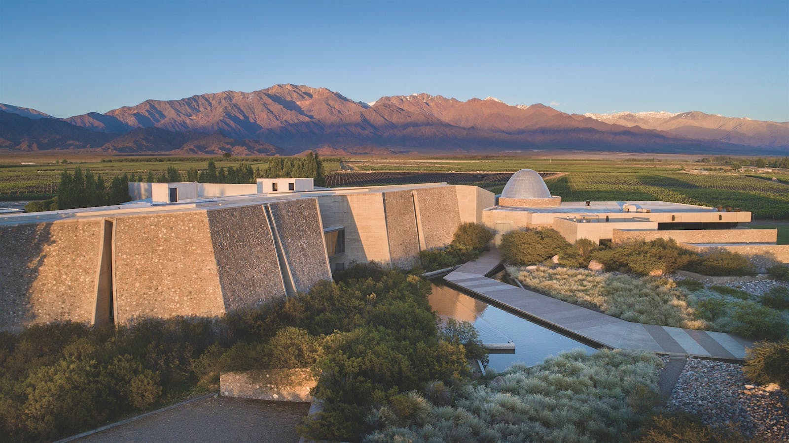 Aerial view of Familia Zuccardi’s winery buildings and estate vineyards in Luján de Cuyo, Mendoza, with the Andes visible in the background.