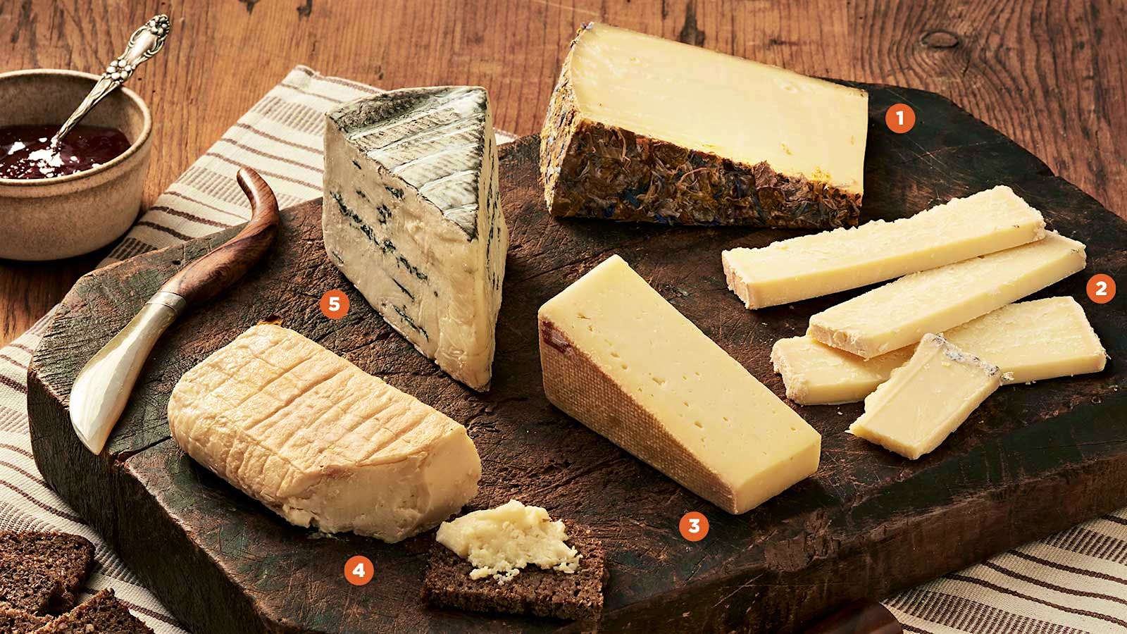 Five cheeses from Germany on a cheese board with knives, pumpernickel toasts and a jelly.